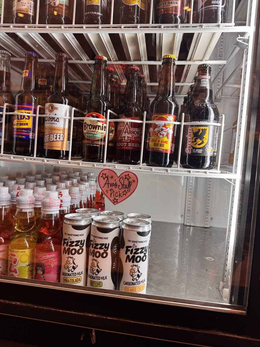 Three Fizzy Moo cans in a store fridge next to other sodas